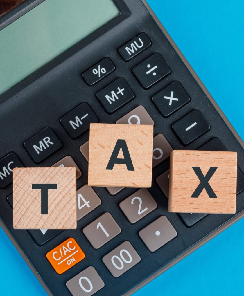 Tax planning concept with wooden cubes on calculator on blue background flat lay.