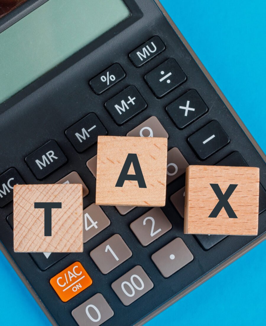 Tax planning concept with wooden cubes on calculator on blue background flat lay.